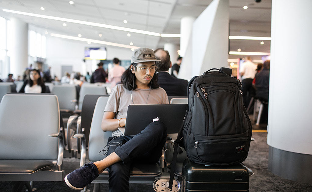 Person working on a laptop in an airport; their Synik 30 is on their rolling luggage.