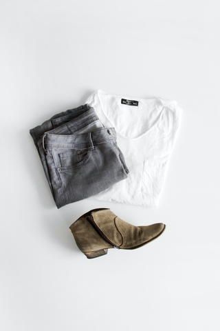 A pair of jeans, shirt, and boots laid out on a white background.