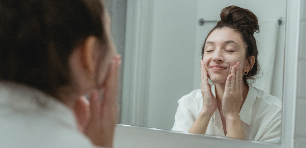 woman applying the best face wash for oily skin in the mirror