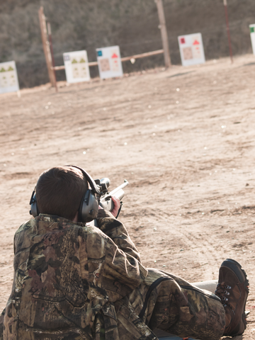 man aiming gun at target while sitting on the ground