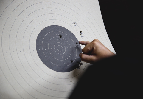 person looking at bullet holes on paper shooting target