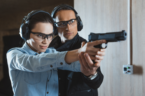 man helping woman aim gun at the shooting range