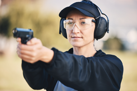 woman with safety equipment aiming gun at an outdoor range