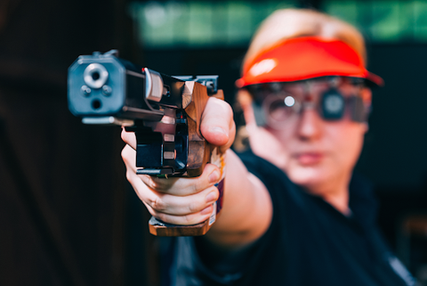 A person pointing a gun wearing a red hat with his finger on the trigger