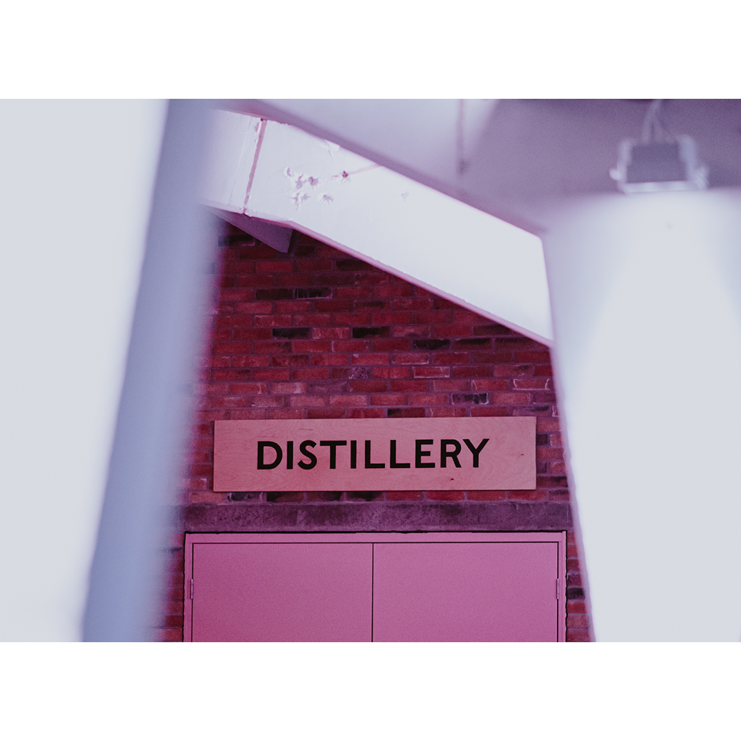 White archway in Sweetdram warehouse with pink distillery doors in the background, and wooden "DISTILLERY" sign above doors.