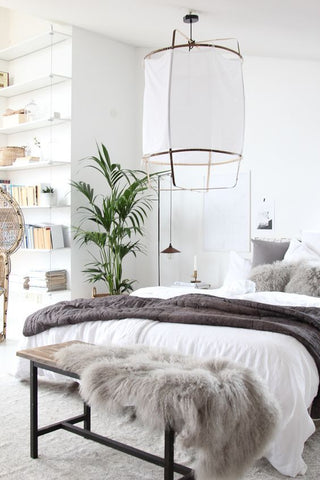 White bedroom with a big hanging lamp and a plant in a Scandinavian home