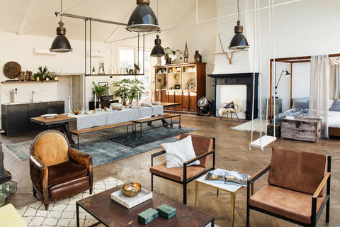 Eclectic interior with black industrial lights, brown leather armchairs, a swing, long dinning table and a 4 poster bed