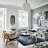 Scandinavian apartment living room interior with greyish green walls, black carpet, wooden armchairs, grey sofa, oval mirror and a round white light