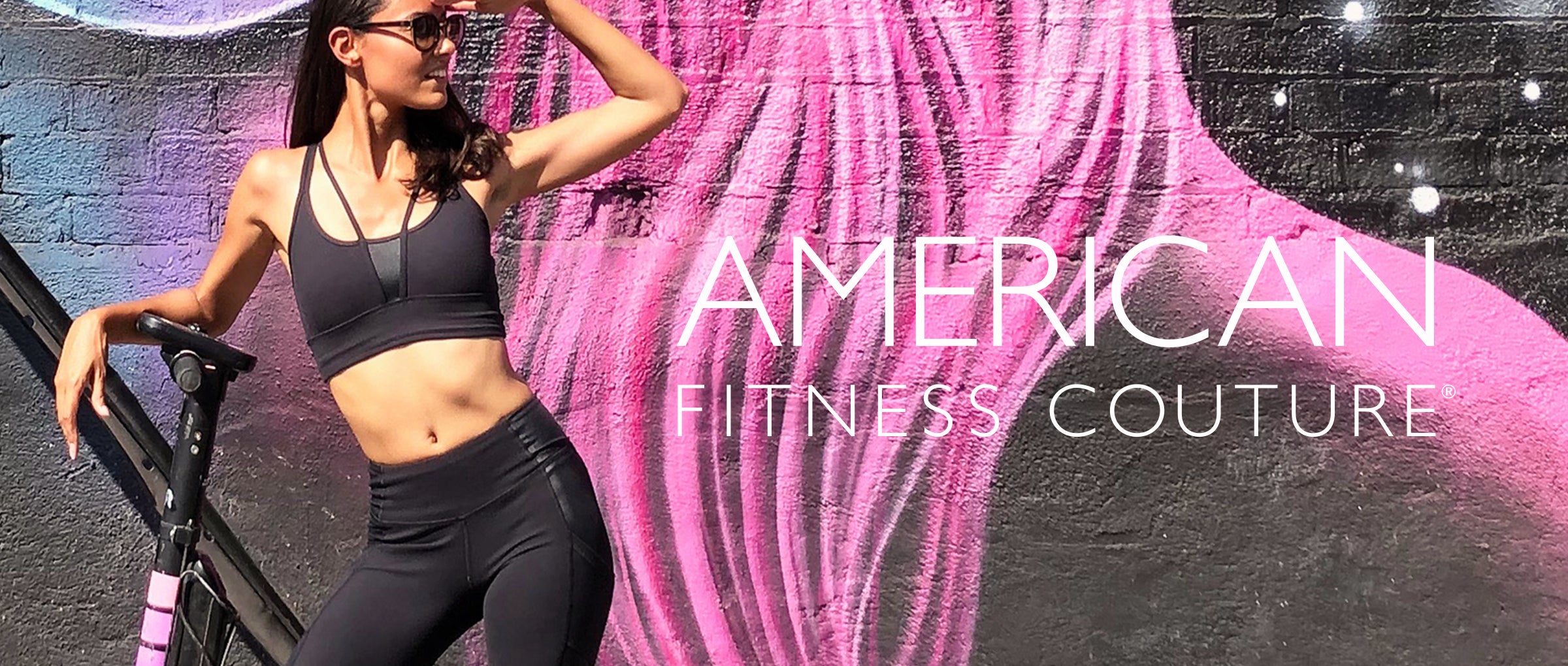 American Fitness Couture Mission | Model wears black leggings and strappy bra in front of graffiti wall.
