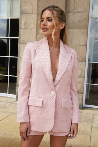 A woman stood outside wearing a blush pink blazer with crystal embellishments.