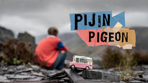 Pijin| Pigeon.  A background of a mining quarry with a miniature toy ice cream van in focus at the front with a boy sitting in the background slightly out of focus. He his wearing a salmon pink rugby jersey.