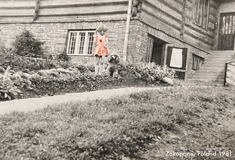 Beata, 9 years old standing in front of the house with her dog Argos, wearing the orange polka-dot dress.