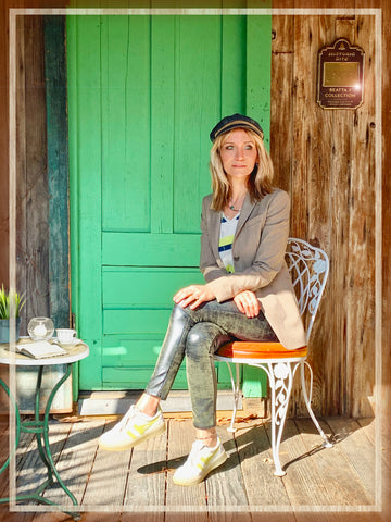 The fashion designer Beata sitting outdoor infront of a green door next to a coffee table wearing stylish clothes