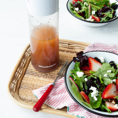 poppy seed vinaigrette in a Whiskware Dressing Shaker sitting on a wicker serving mat with a fresh salad