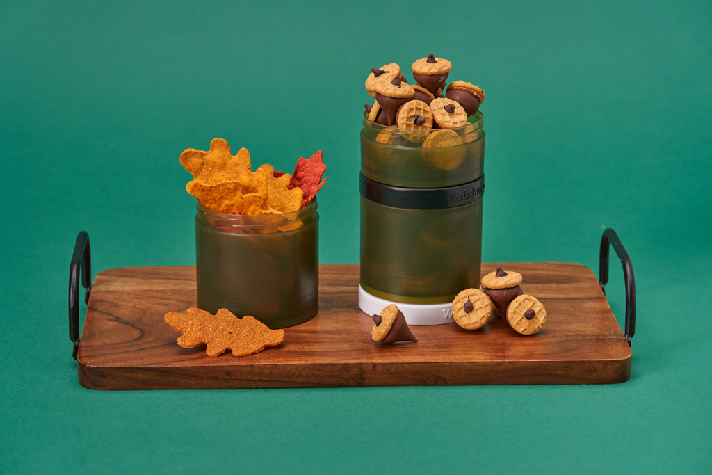 a dark green whiskware snack container filled with fall inspired goodies like leaf chips and hershey kisses