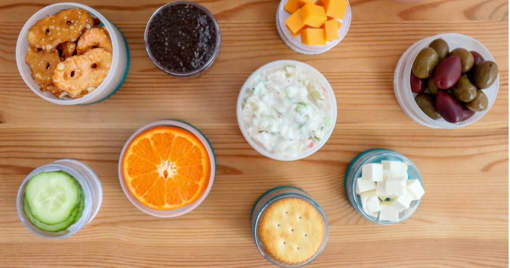 A collection of 9 snacking containers filled with various fruits, vegetables, and other healthy snacks.