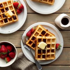 waffles on a plate with syrup on top garnished with strawberries. everything is sitting on a wooden table