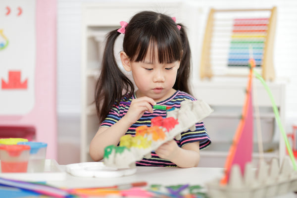 A young girl painting an egg carton