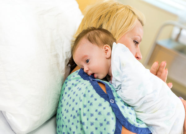 Newborn baby being burped over mother's shoulder in hospital