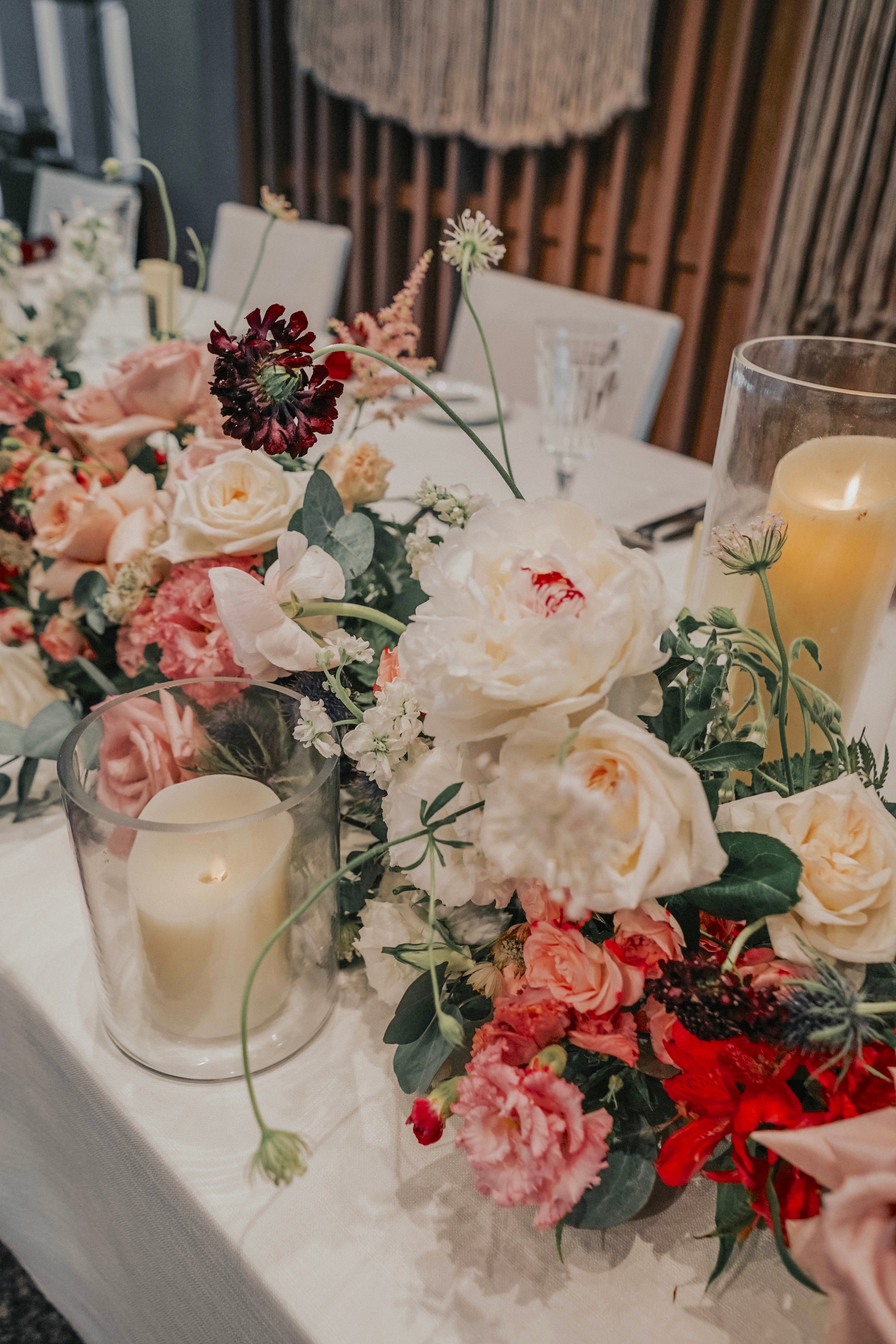 Close up of white peony and off-red eustomas tucked among lush greenery as a floral table garden with lit candles 