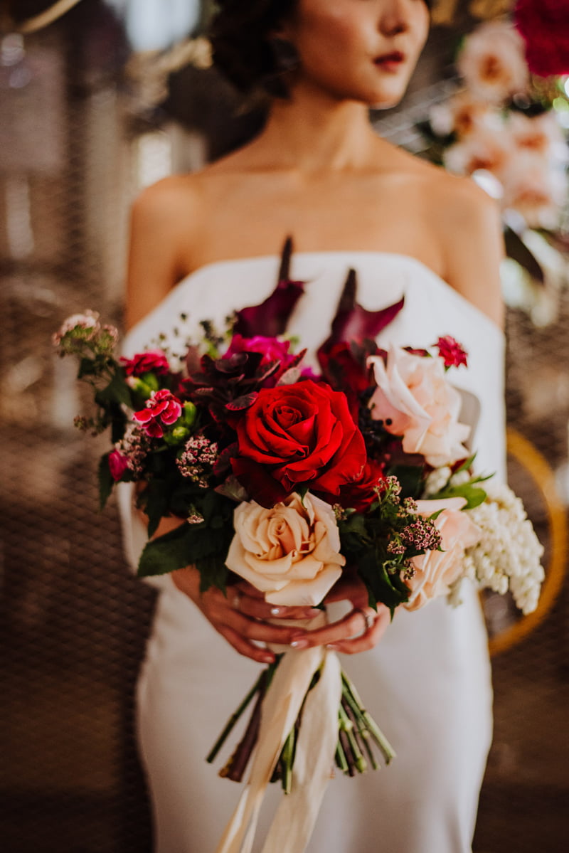 Bride holding out a bouquet of verdant, plush blooms, tied with a pale pink ribbon