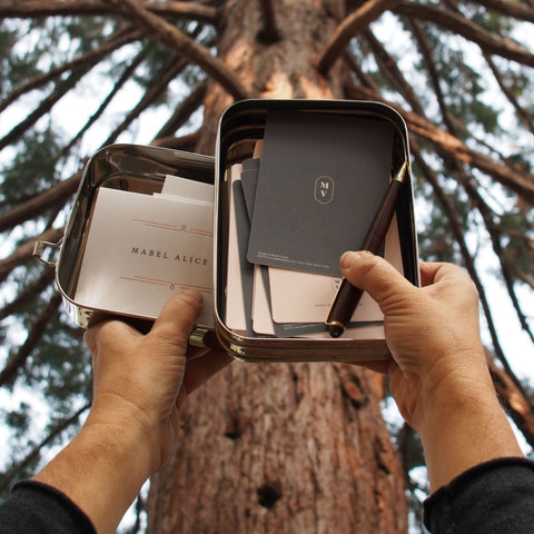 Solo Rectangle ECOlunchbox holding a pen and stationery held up near a tall tree.
