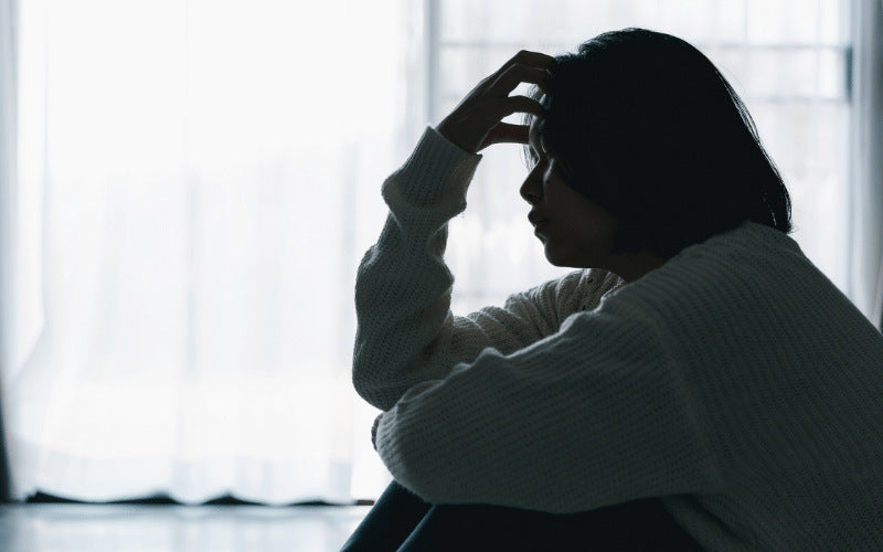 depressed teenage girl sitting in the dark with her hand on her head