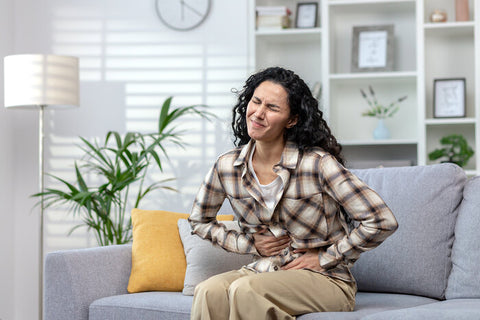 mature woman on couch holding her abdomen in pain