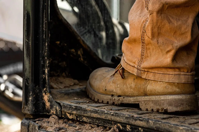 brown work boot of a construction worker sitting on an aged dirty tractor