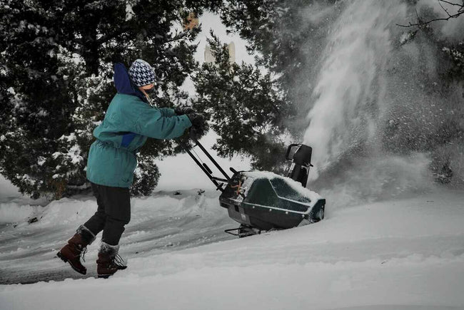 a woman in winter work gloves and full equipment cleans snow with a machine