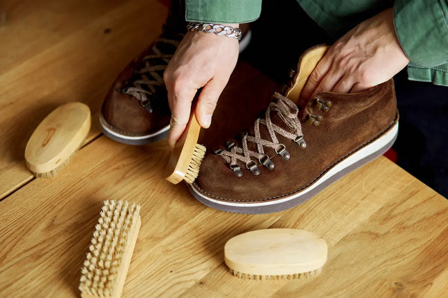 man's hand clean suede shoes, boots with a brush on wooden background