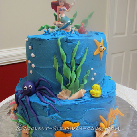 strands of seaweed, an octopus, fish, shells, and a starfish on a simple blue frosted cake. mermaid