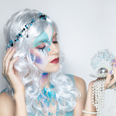 Woman with colourful mermaid makeup holding a white shell with a pearl inside