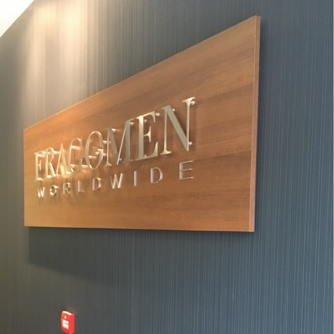 Reception sign at Fragomen Dublin featuring a walnut panel and brushed stainless steel lettering fixed to the wall to give a floating illusion. Signage by Barrow Signs