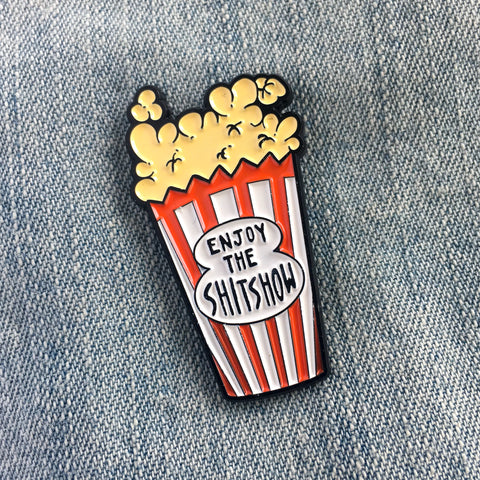 A funny enamel pin of a bag of popcorn with the quote, "Enjoy the Shitshow"