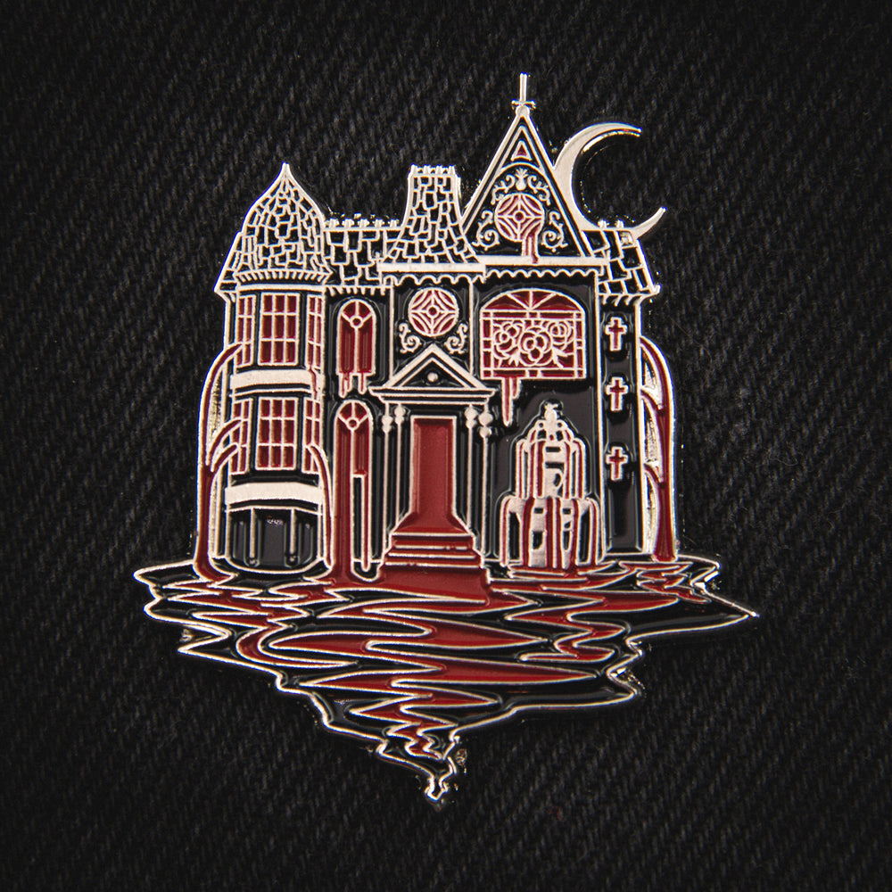 A beautiful, detailed enamel pin of a Victorian mansion pouring blood from its windows and doors. Made from silver metal with black and red enamel. 