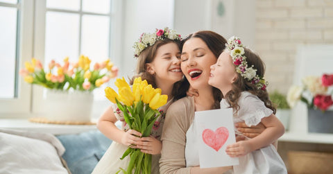 Celebrating Motherhood - Two young girils presenting their mom a card and a bouquet of flowers