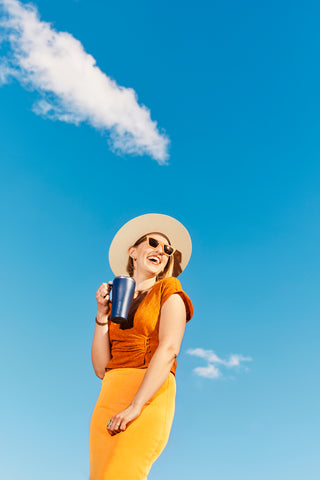 woman smiling and holding coffee tumbler outside.