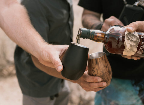 person pouring whiskey into drink tumblers.