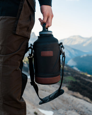 person holding a drink tumbler by mountains.