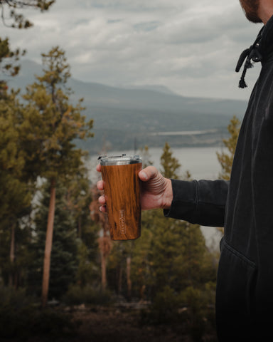 person holding tumbler in mountains.