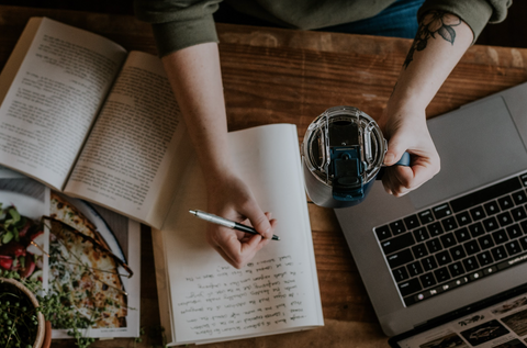 person writing on a notebook at a coffee table.