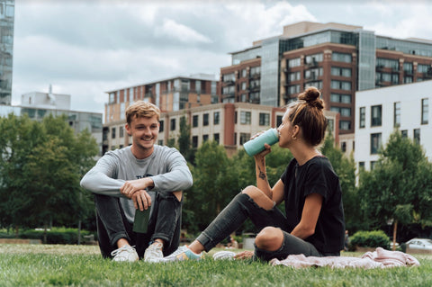 man and woman sitting in the grass with their tumblers.