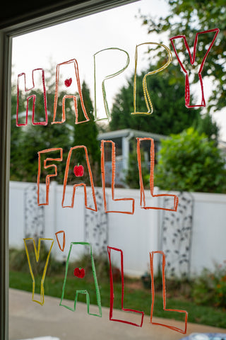 Window decorated for Halloween and fall that says "Happy Fall Y'all".