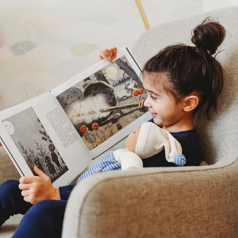 A young boy sits reading his favorite book with his cuddly companion.