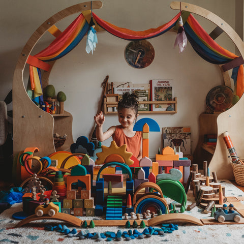 A young child sits amongst a collection of Grimm's Wooden Toys.