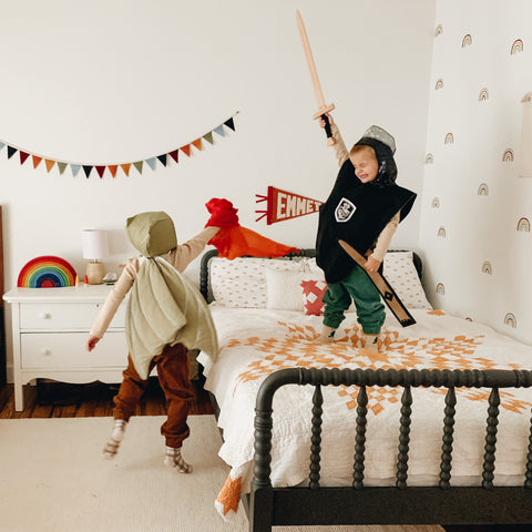 Two young children are dressed up as a knight and a dragon playing in a bright room.