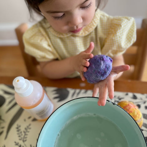Small child rolling wool in an egg shape between her hands to make a wet felted wool easter egg