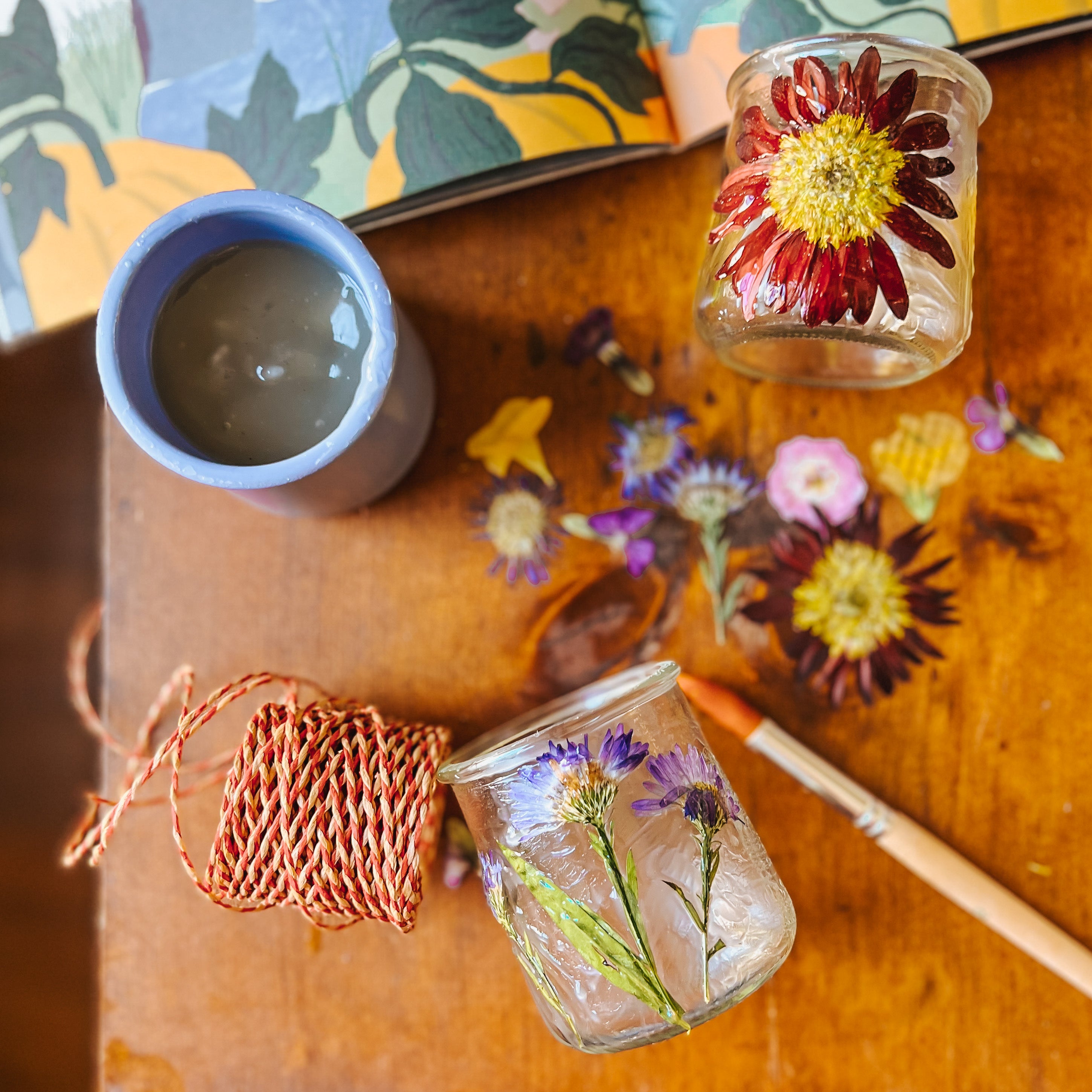 Glass jars sit on a table with pressed flowers.
