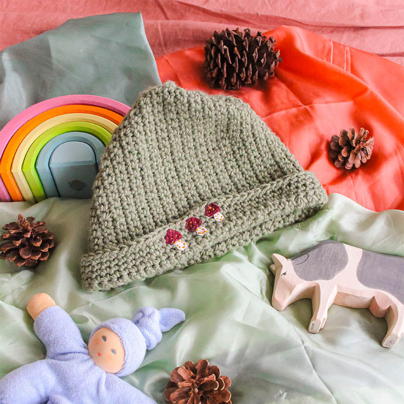 A simple crochet hat sits on a playsilk with Waldorf toys.